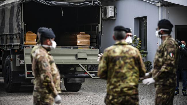 Italian soldiers wait for coffins they took from the Bergamo area are unloaded at a cemetery near Milan in Northern Italy. Picture: AP