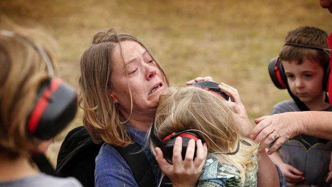 A distressed mother convinces her child to wear hearing protection before being airlifted out of Mallacoota in a Chinook army helicopter. Picture: David Caird