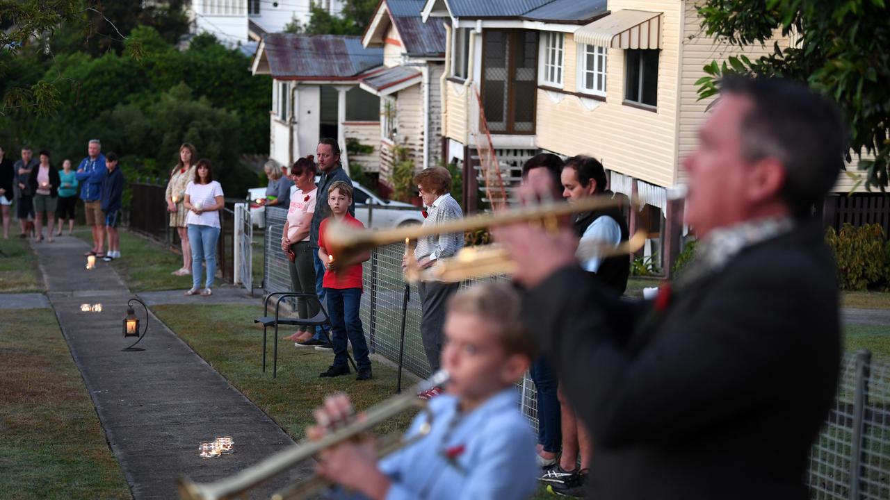 Alastair Tomkins and his nine year-old son Hugo play The Last Post in their driveway, at dawn, as neighbours stand outside their homes to commemorate Anzac Day in Brisbane. Picture: Dan Peled