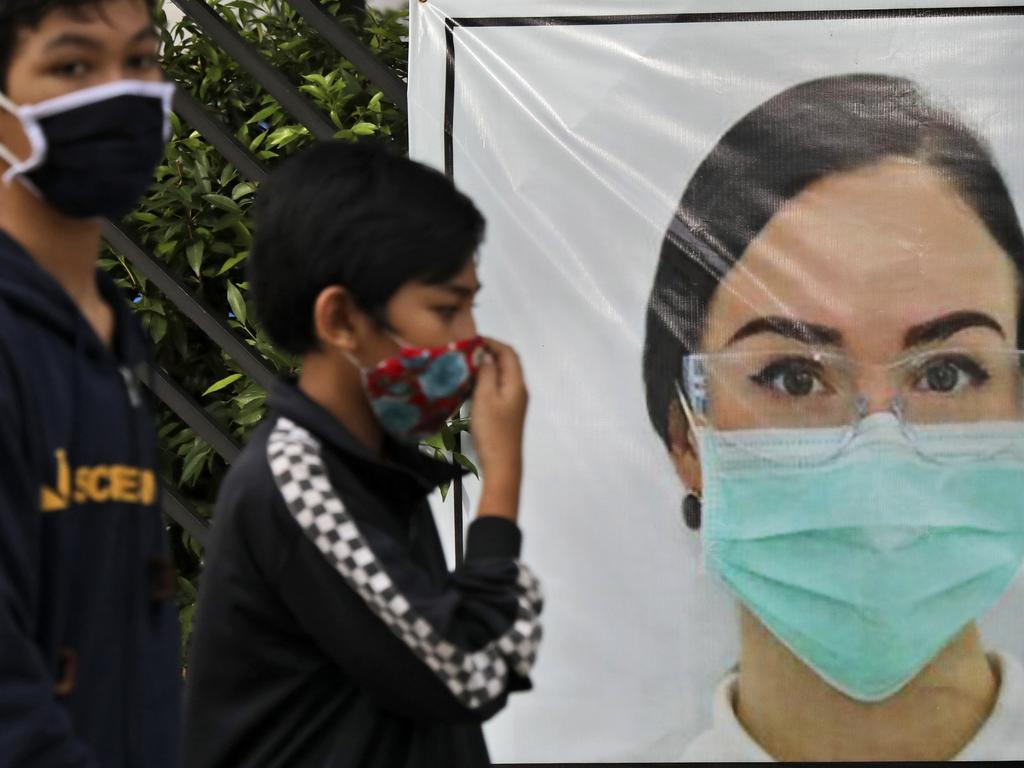 Indonesian youths walk past a banner that calls for people to always wear face mask as a precaution against the new coronavirus outbreak, in Jakarta, Indonesia. Picture: AP Photo/Dita Alangkara