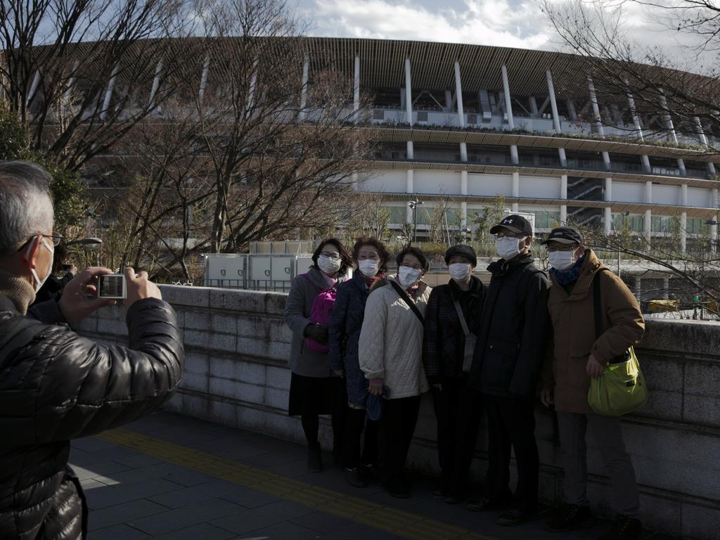 Tourists wear masks as they pause for photos with the New National Stadium in Tokyo