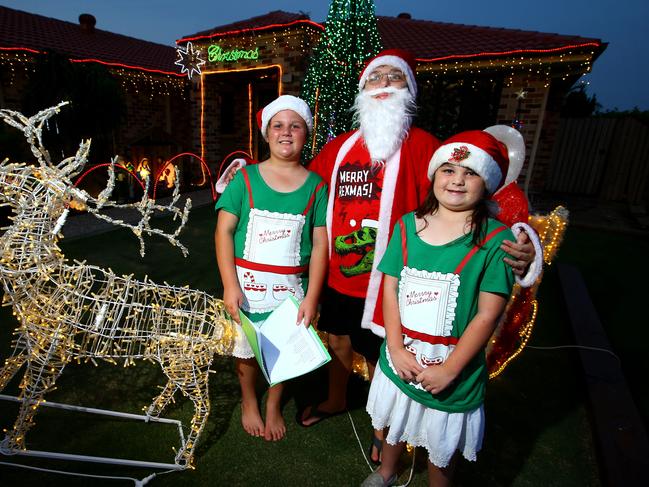 Upper Coomera residents Brianna Corcoran and Georgia Thistlethwaite sing carols for visitors with Santa’s helper Jacob Corcoran Photo: David Clark