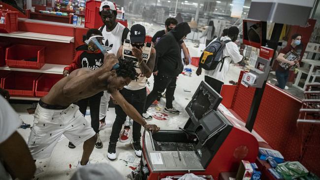 A looter uses a claw hammer to break into a cash register at a Target store in Minneapolis. Picture: AP