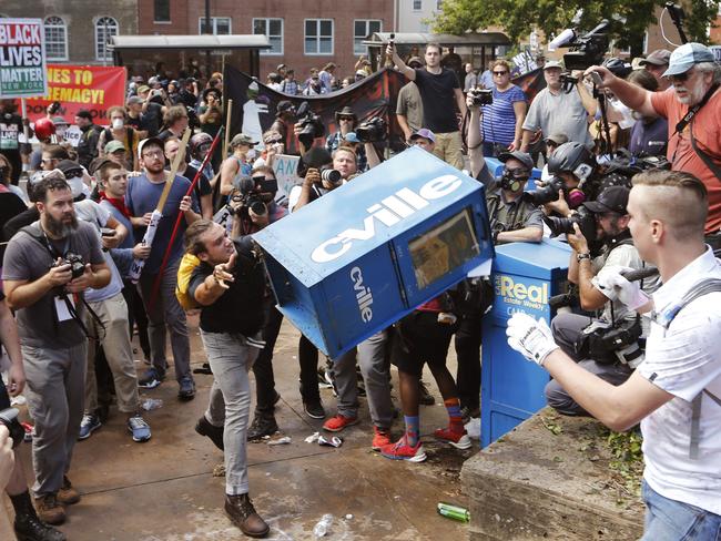 White nationalist demonstrators clash with a counter-demonstrator as he throws a newspaper box at the entrance to Lee Park in Charlottesville, Virginia on Saturday. Picture: AP Photo/Steve Helber