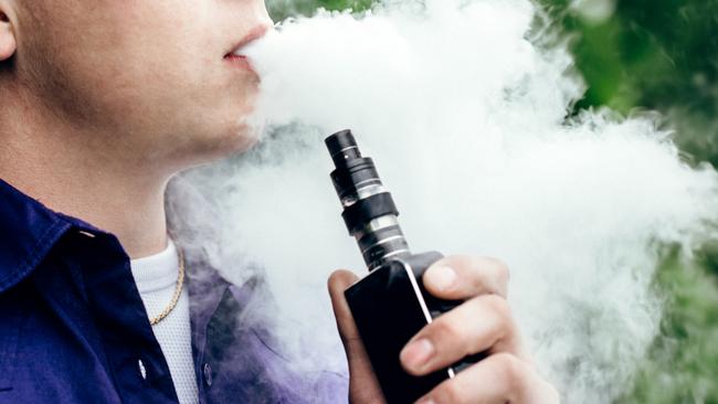 A young adult male has a cloud of nicotine vapor "smoke" pouring from his mouth.  Vape smoking, or "vaping" is growing in popularity, as well as falling under stricter state and governmental regulations.  Horizontal image with copy space.