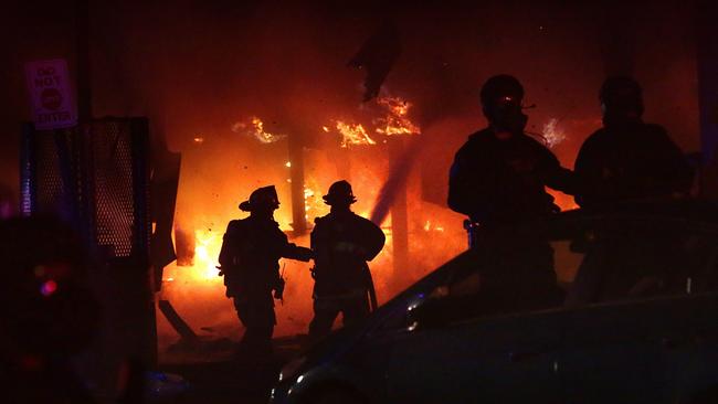 St. Louis firefighters are protected by police as they put out a fire at at looted 7-Eleven convenience store. Picture: AP