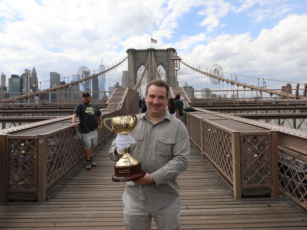 Australian race caller Matt Hill and the Lexus Melbourne Cup trophy on Brooklyn Bridge. Picture: TJ Balkun