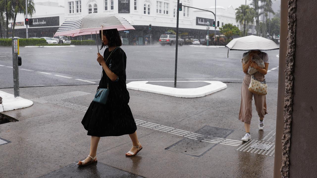 Two women walk along Spence Street in the pouring rain, sheltering under umbrellas, as unrelenting wet weather to Cairns. Picture: Brendan Radke