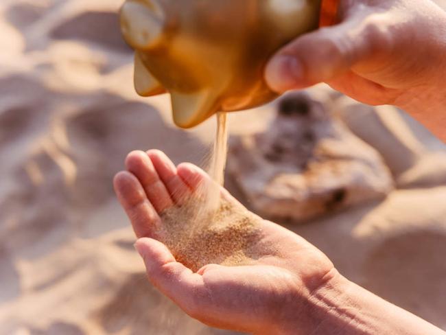 Hand holding golden piggy bank with sand coming out.