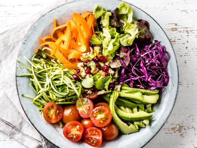 Vegan buddha bowl. Bowl with fresh raw vegetables - cabbage, carrot, zucchini, lettuce, watercress salad, tomatoes cherry and avocado, nuts and pomegranate on white background