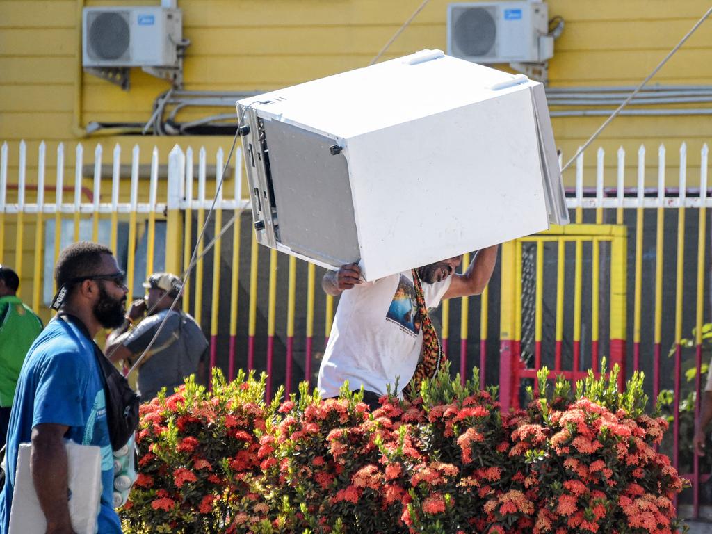 A man carries a freezer as crowds leave shops with looted goods. Picture: AFP