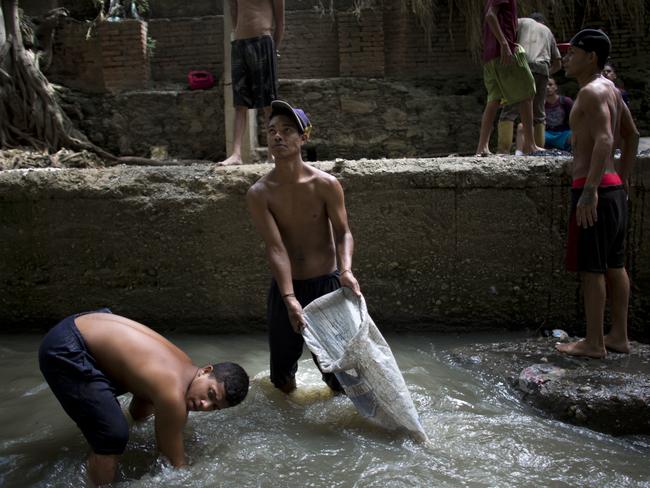 In this Nov. 30, 2017 photo, Douglas, center, holds a sack in the polluted Guaire River as he and others pull mud up from the bed of the river in search of gold and other valuables to sell, in Caracas, Venezuela. The river and the scavengers in it go largely unseen by Caracas residents speeding overhead on the city's main highway, blocked from view by concrete barriers. (AP Photo/Ariana Cubillos)