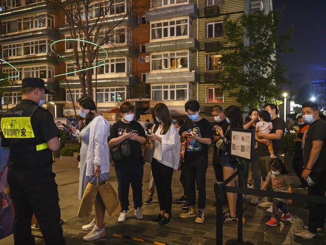 Shoppers line up to scan their local health odes from the Beijing Municipality before entering a shopping area in Beijing.