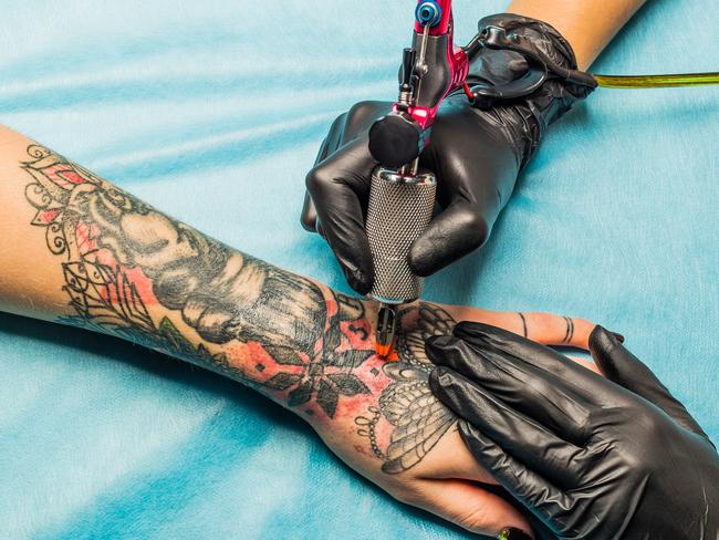 Close up tattoo artist demonstrates the process of getting black and red tattoo with orange paint. Master works on the professional blue mat in black sterile gloves.  - Picture istock