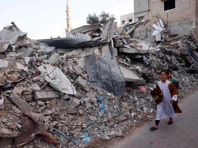 Young Palestinian boys carry their prayer mats as they walk past a destroyed building on their way perform the Eid al-Adha morning prayer in al-Bureij in the central Gaza Strip. Picture: AFP