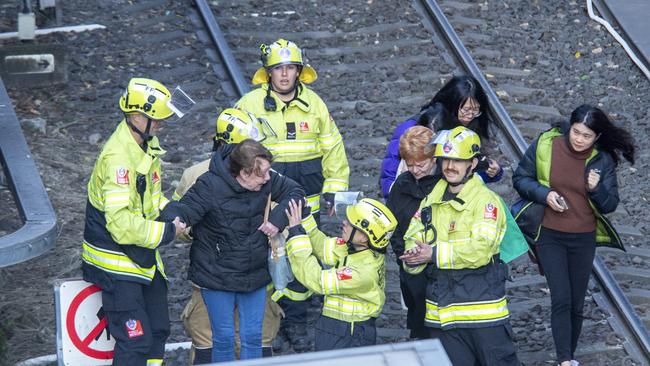 Passengers are escorted by emergency services along the light train rail line after being trapped by a fallen tree. Picture: NewsWire / Jeremy Piper