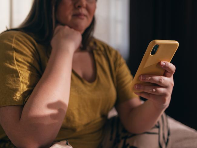 An unrecognizable plus size woman in a yellow T-shirt watching reels on her mobile phone.