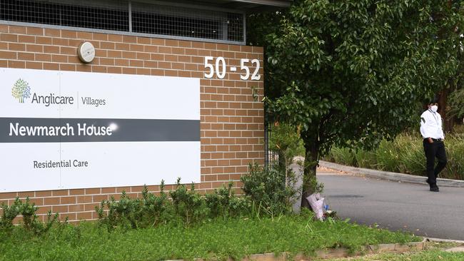 A security guard stands in the driveway as flowers are seen left at the entrance to Anglicare Newmarch House agedcare home in Kingswood, near Penrith.