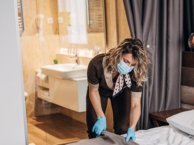 One woman, beautiful maid with medical mask changing bed linen on the bed in a hotel room.