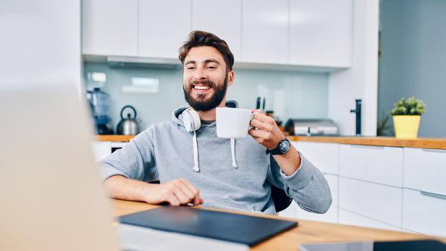 Joyful young web developer drinking coffee while taking break from work in home office