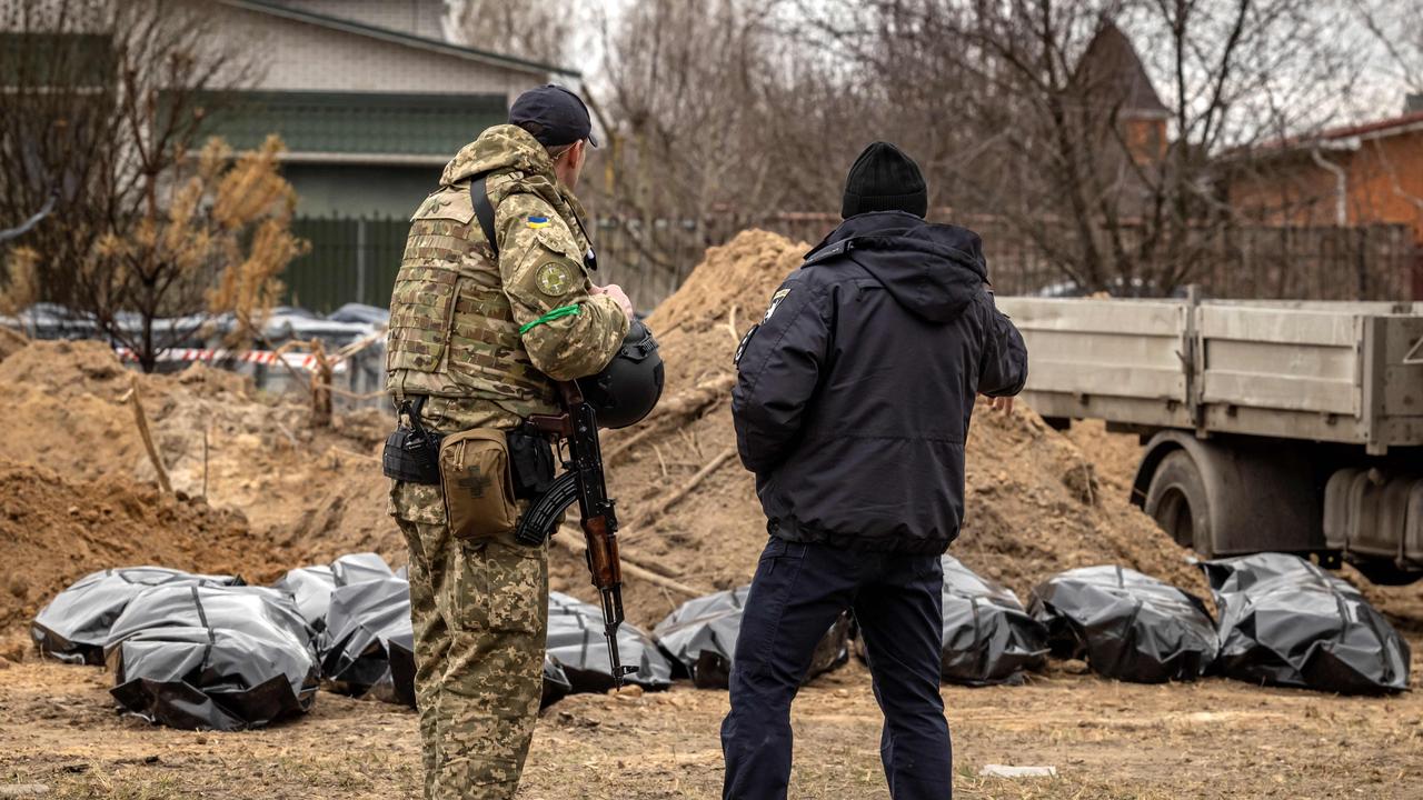 A member of the Ukrainian army and a policeman stand near body bags exhumed from a mass grave in Bucha, on the outskirts of Kyiv. (Photo by FADEL SENNA / AFP)