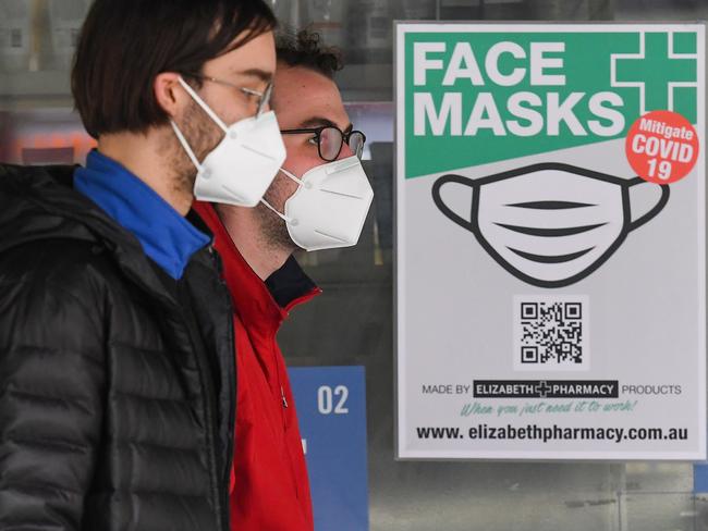 People wearing face masks walk past a sign advertising masks in Melbourne on July 20, 2020. - Australia's second-biggest city will make it compulsory to wear a mask in public, authorities announced on July 19, as Melbourne steps up efforts to bring a coronavirus outbreak under control. (Photo by William WEST / AFP)