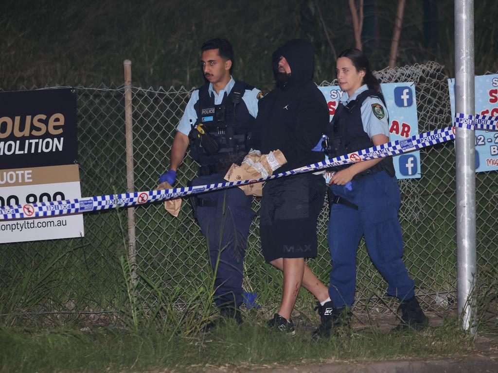 Samimjan Azari, who was inside the car that was shot at, is led away from the crime scene at Granville under the M4 overpass. He has since been charged with firearm offences. Picture: Rohan Kelly