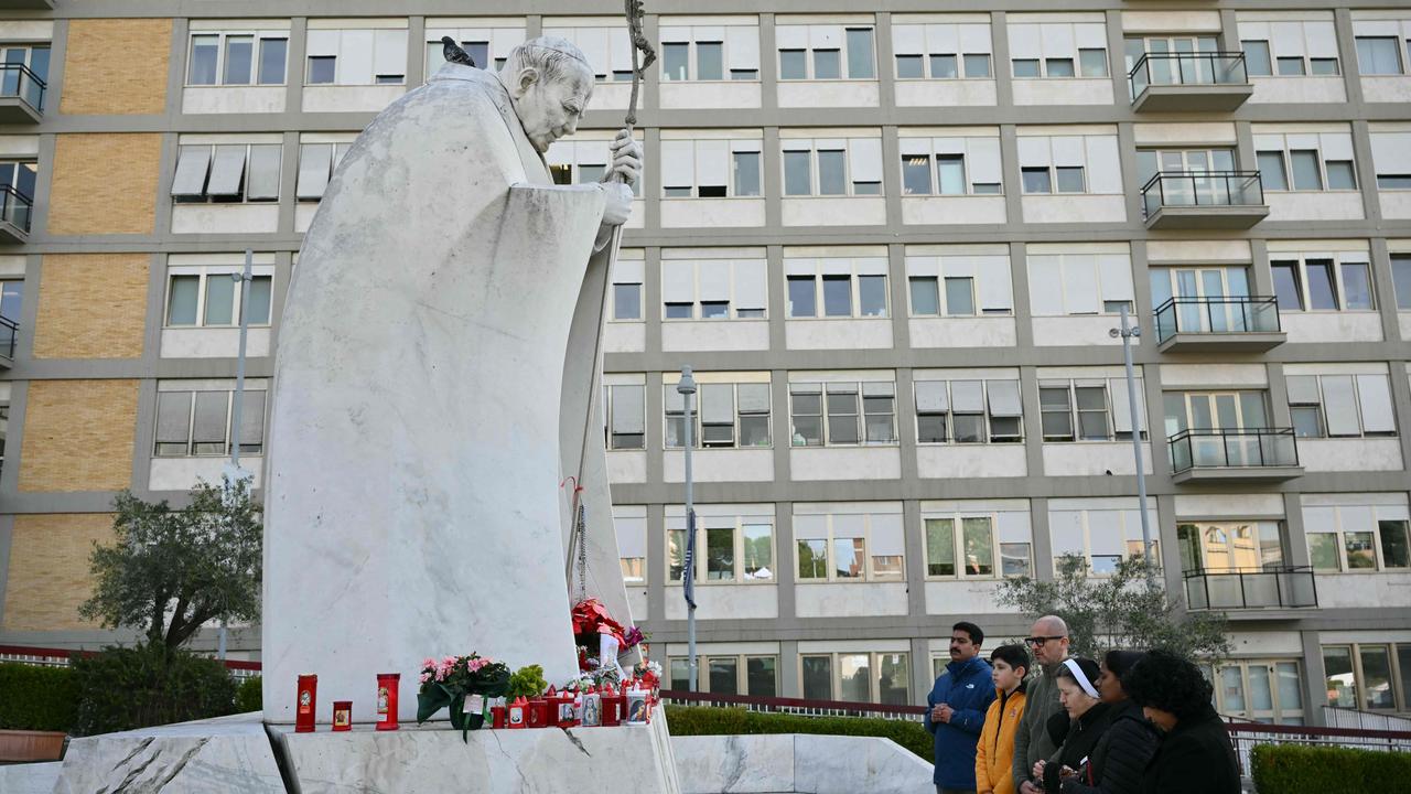 People pray at the statue of John Paul II outside the Gemelli hospital where Pope Francis is hospitalised for pneumonia. (Photo by Alberto PIZZOLI / AFP)