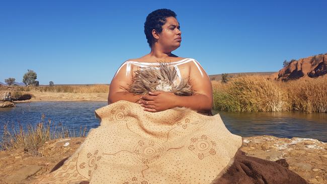 Breaking Ground award winner Juanella McKenzie with two of her works made from emu feathers and kangaroo skin, at Pungka Pudinah (Hookina Waterhole) in the Flinders Ranges, photographed by her husband Michael Donovan.