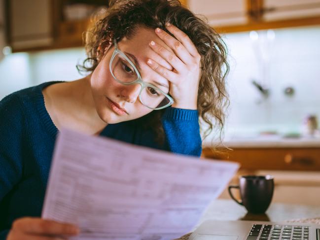 Young brunette curly female reading her bill papers, looking stressed. Picture:  iStock.