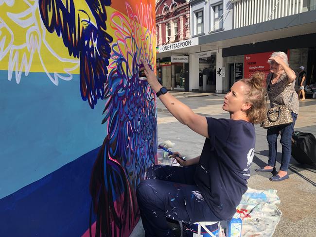 Mona Vale artist Meg Minkley working on Friday morning on her temporary mural – as a curious local looks on – to be installed on The Corso at Manly as part of Northern Beaches Council's support of the international WorldPride LGBTQIA+ festival. Picture: Jim O'Rourke