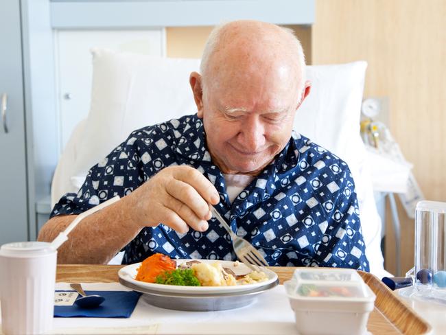 Senior male patient in hospital eating a meal â head and shoulders with generic equipment looking down. Some motion blur.