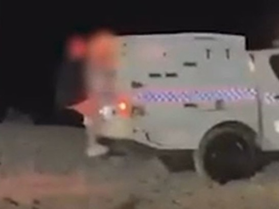 A teenager rides on the exterior of a police car at Schoolies on the Gold Coast in a screenshot from a social media video.