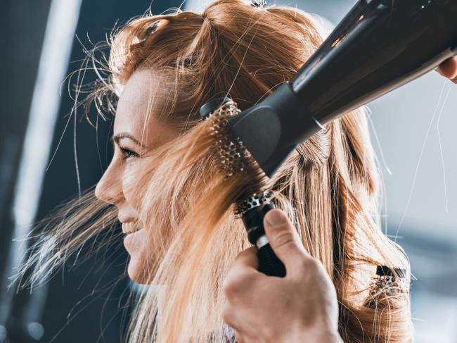 Young hairdresser drying customers hair with round brush at hair salon. Hairdresser generic