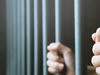 Man in prison hands of behind hold Steel cage jail bars. offender criminal locked in jail.