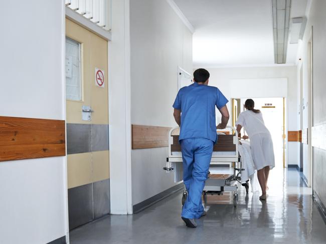 Rearview shot of hospital staff wheeling a patient in a gurney down a corridor