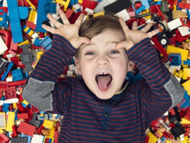 A little happy blond boy with blond hair and blue eyes lies between a lot of colorful plastic blocks toy / building blocks.