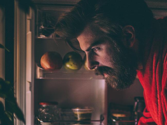 Bearded man in bathrobe opening beer can in front of the refrigerator