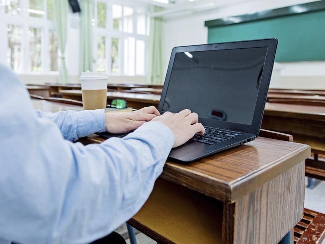 Male student typing on laptop in his classroom.