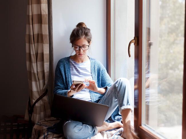 CORONAVIRUS: Picture: istock Young woman working from home office. Freelancer using laptop, phone and the Internet. Workplace in living room on windowsill. Concept of female business, career, shopping online. Lifestyle moment.