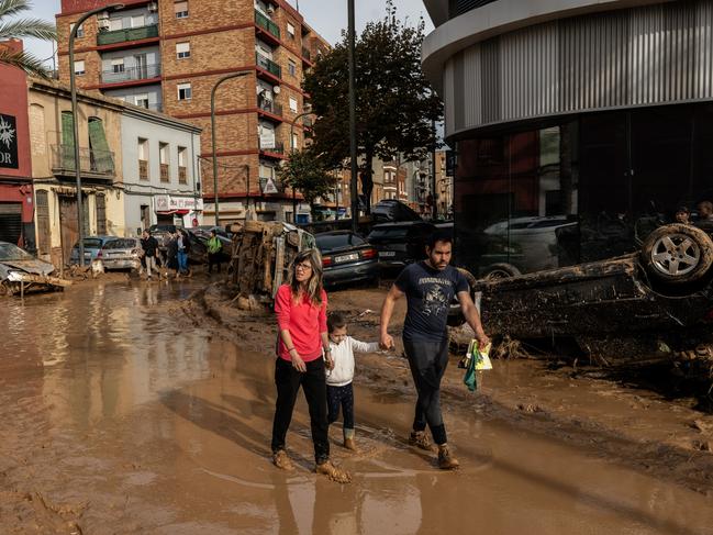 A family walk through muddy waters in a street after the recent flash flooding in the Alfafar municipality of Valencia, Spain. Picture: Getty