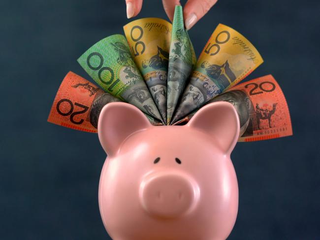 Pink Piggy bank money concept on dark blue background, stuffed with Australian cash, and female hand take one hundred dollar note.