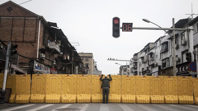 A man wearing a face mask talks to another man through a makeshift barricade wall built to control entry and exit to a residential compound in Wuhan in March. Picture: Getty Images