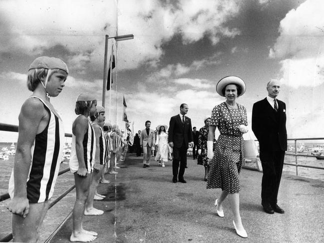 The Queen admires members of her little honour guard, members of the Nippers movement of the Surf Life Saving Association, as she is escorted down Glenelg jetty by the Deputy Governor, Mr. W. Crocker, and followed by Prince Philip, walking with Lady Nicholls, wife of the Governor, Sir Douglas Nicholls, and the Premier Don Dunstan and his wife Adele Koh.