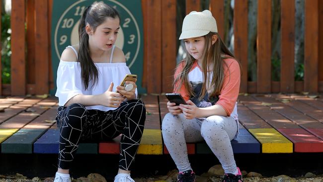 Primary school students Ruby and Lia at Brisbane’s New Farm Park with their mobile phones. Education experts are calling for a blanket ban on all mobile phones in primary schools. Picture: David Clark/AAP