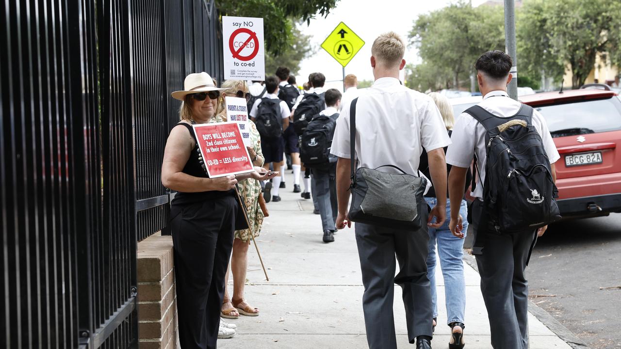 Students walk past signs protesting against Newington College’s decision to start accepting girls from 2026. Picture: Richard Dobson