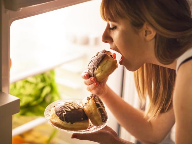 Picture: iStockClose up image of a young woman with eating disorder, having a midnight snack - eating donuts, in front of the refrigerator.