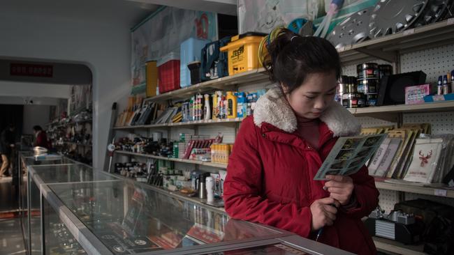 A sales assistant looks at a leaflet as she waits for customers at a vehicle parts shop in Pyongyang on November 16, 2017. Picture: AFP / Ed Jones.