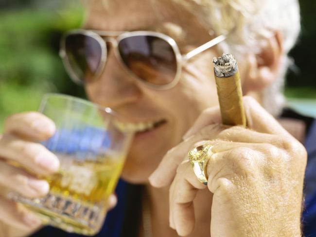 Middle aged adult man holding a glass of whiskey alcoholic drink and a smoking cigar.