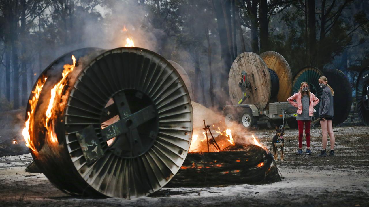 Two sisters walk their dog among burning NBN cable rolls in Mallacoota last month. Picture: David Caird